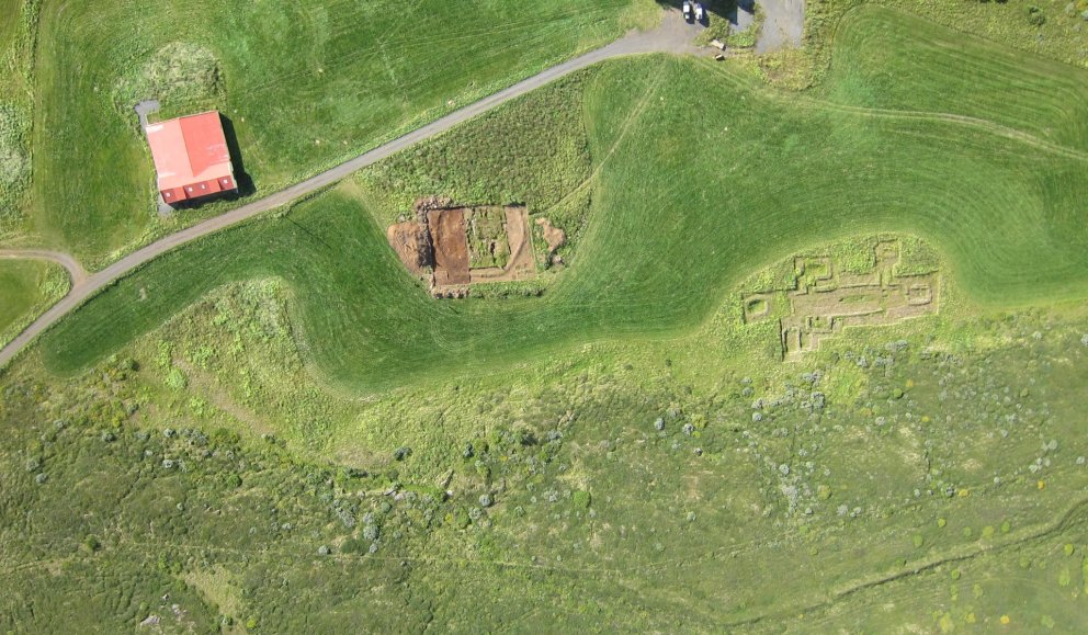 Loftmynd tekin með þyrlu, austan við túnið, sem sýnir afstöðu kirkjugarðsins gagnvart núverandi bæjarhúsum á Hofstöðum og rúst víkingaaldarskálans í ágúst árið 2013. ©Fornleifastofnun Íslands ses.
